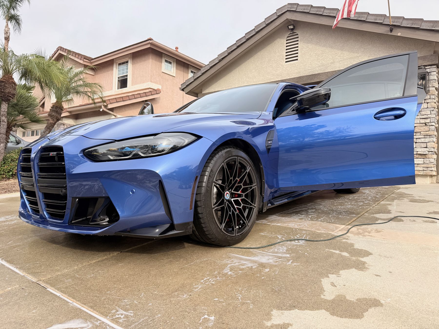 Freshly washed blue BMW M4 Competition gleaming in a driveway during a mobile detail